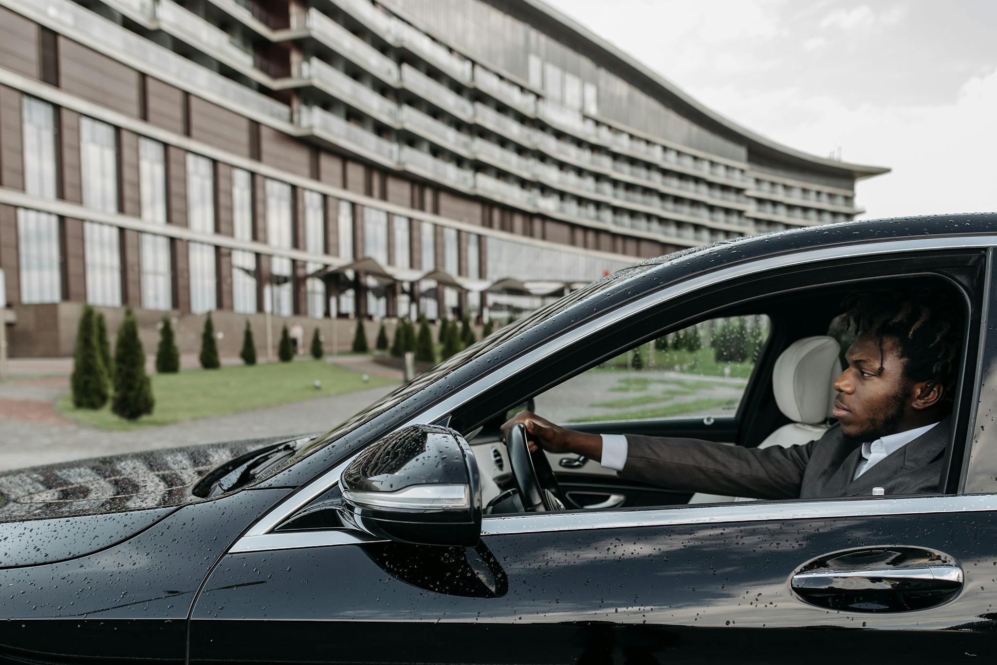 Black man driving a luxury vehicle in front of a modern building, exuding confidence.